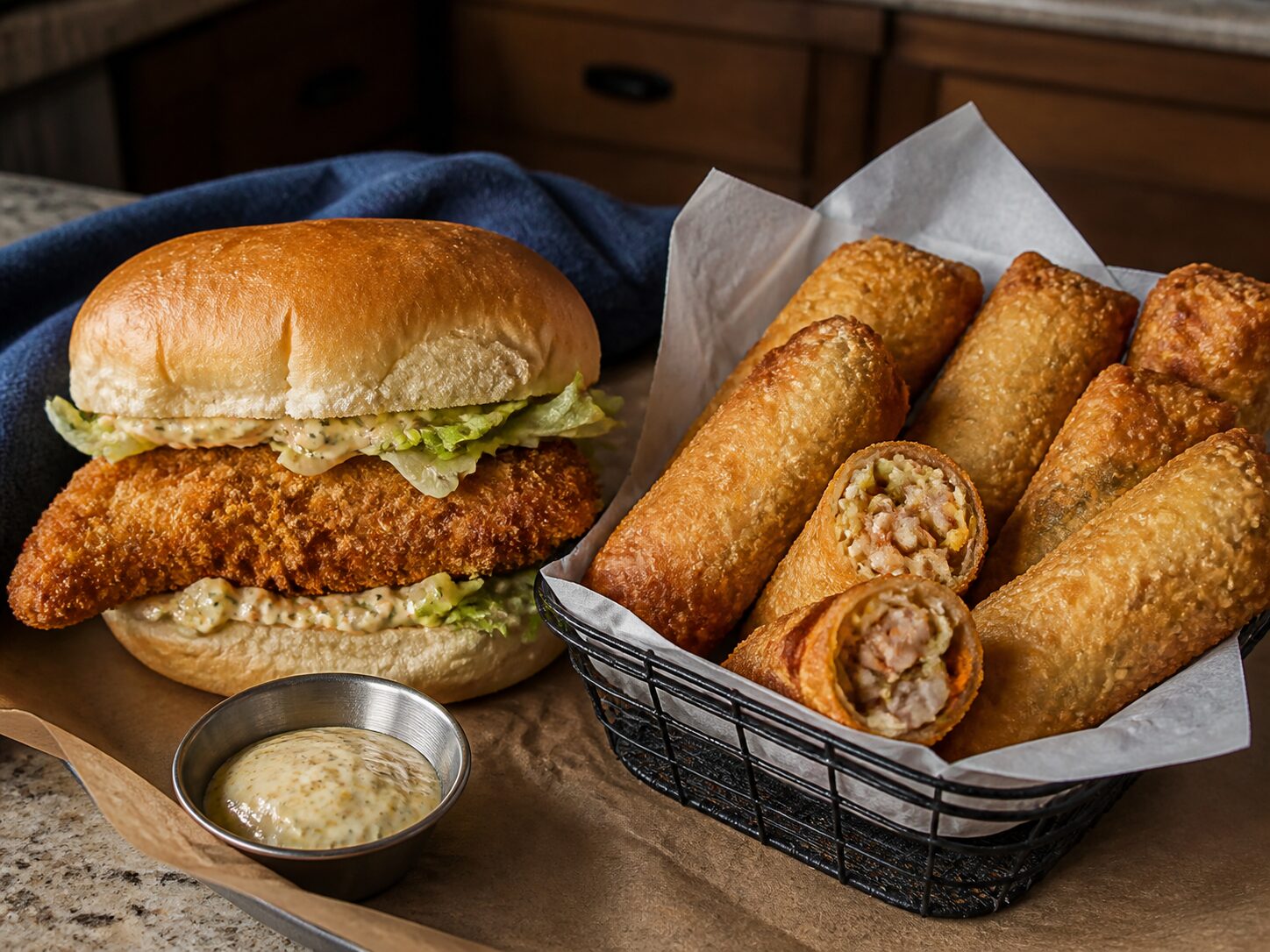 Fried chicken sandwich beside a basket of golden-brown egg rolls with dipping sauce